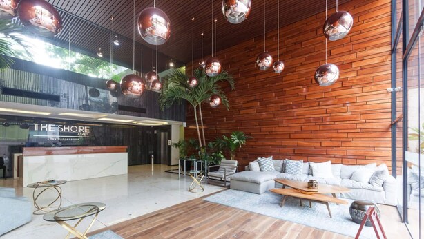 Eine moderne Lobby mit einer Rezeption, einer Couch, einem Couchtisch und hängenden, kugelförmigen Leuchten.