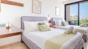 Ein Hotelzimmer mit zwei Betten, einem Schreibtisch und einem großen Fenster mit Blick auf die Stadt.