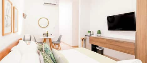A hotel room with a bed, a desk, a chair, a television, and a small table with a bottle and glasses.