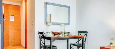 A dining area with a wooden table, two chairs, a mirror, and a small potted plant.