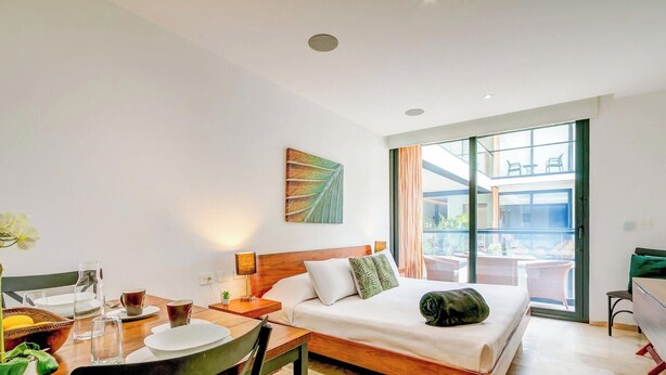 Een hotelkamer met een bed, een eettafel met stoelen, een raam met uitzicht en een schilderij aan de muur.