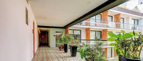 Ein Korridor mit Musterfliesen führt zu einem Balkon mit Blumentöpfen und Blick auf ein Gebäude mit Balkonen.