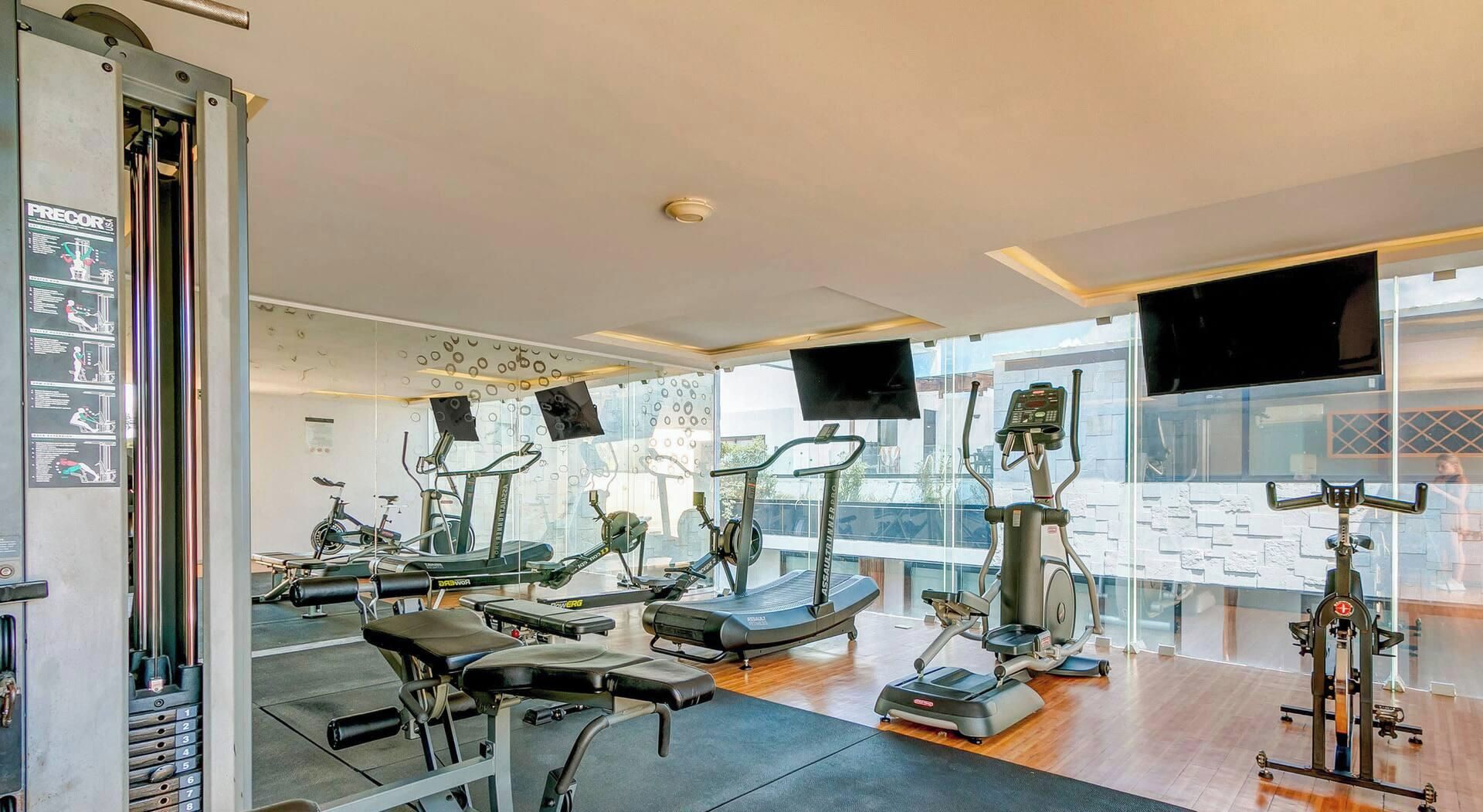 A gym with various exercise equipment, large windows, and a visible staircase.