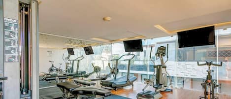 Un gimnasio con diverso equipo de ejercicio, ventanas amplias y una escalera visible.