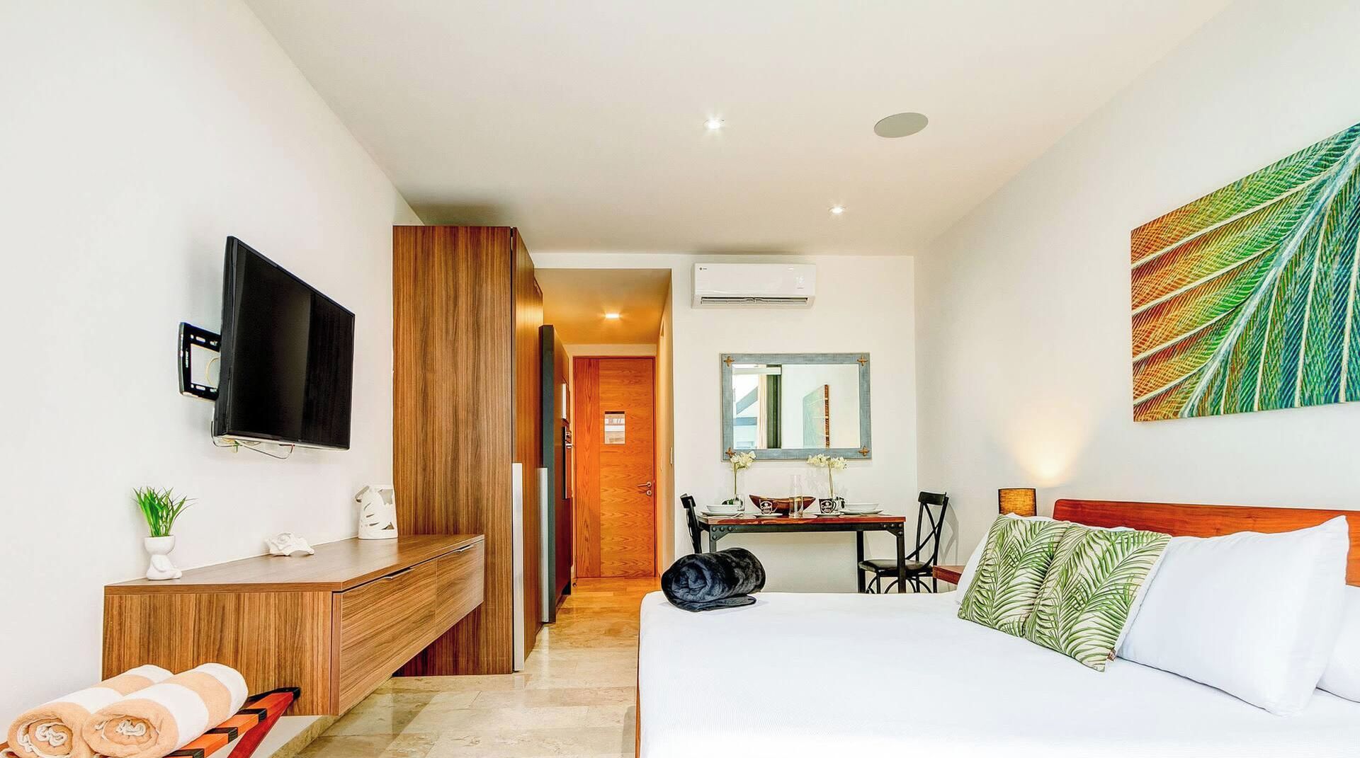 A hotel room with a bed, a desk, a chair, a TV, and a painting.