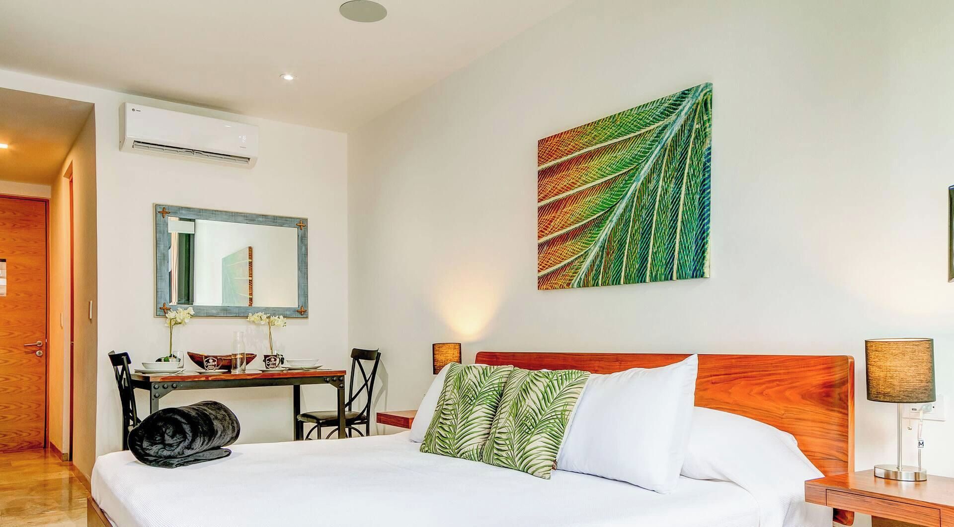 Une chambre d’hôtel équipée d’un lit, d’un bureau, d’une chaise, d’un miroir et d’un climatiseur fixé au mur.