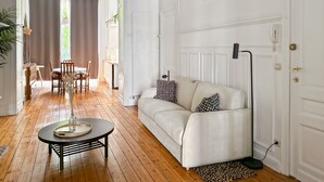 A living room with a sofa, a coffee table, a floor lamp, a dining area with chairs and a table, and a door with a phone. - Brugman Area Self Check in Apartment for 5 (Brussels)