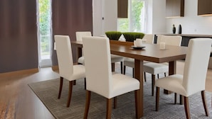 A modern dining room with a wooden table, white chairs, and a view of greenery outside. - Brugman Area Self Check in Apartment for 5 (Brussels)