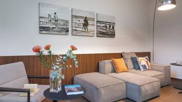 Un salon moderne avec un canapé d’angle gris, une petite table d’appoint sur laquelle se trouvent un livre et un vase de fleurs, et trois tableaux en noir et blanc accrochés au mur.