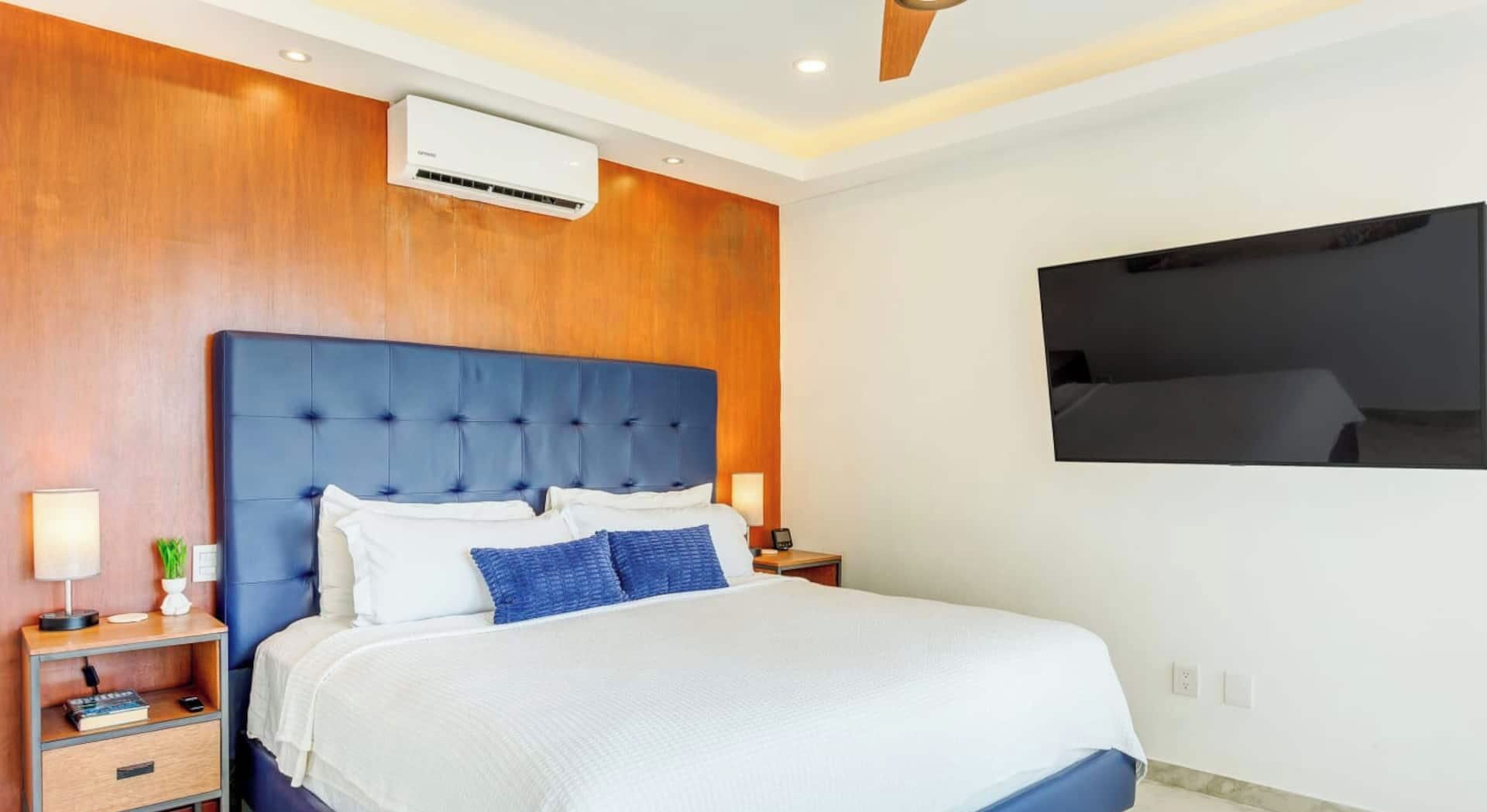Ein Hotelzimmer mit einem großen Bett, einem an der Wand befestigten Fernseher, einem Deckenventilator und einer Klimaanlage.