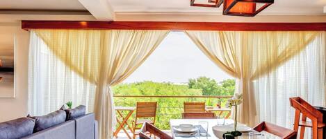 A dining area with a table set for two, a sofa, and a view of greenery.