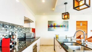 A modern kitchen with a glass backsplash, stainless steel appliances, and a contemporary pendant light. - Beachside retreat w/ rooftop pool & BBQ (Playa del Carmen)