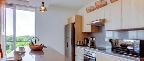 A modern kitchen with a large island, stainless steel appliances, and a view of greenery outside.