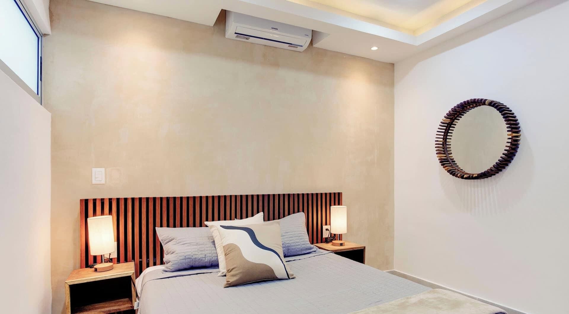 Une chambre moderne comprenant un lit, deux tables de chevet, un miroir fixé au mur et un appareil de climatisation.