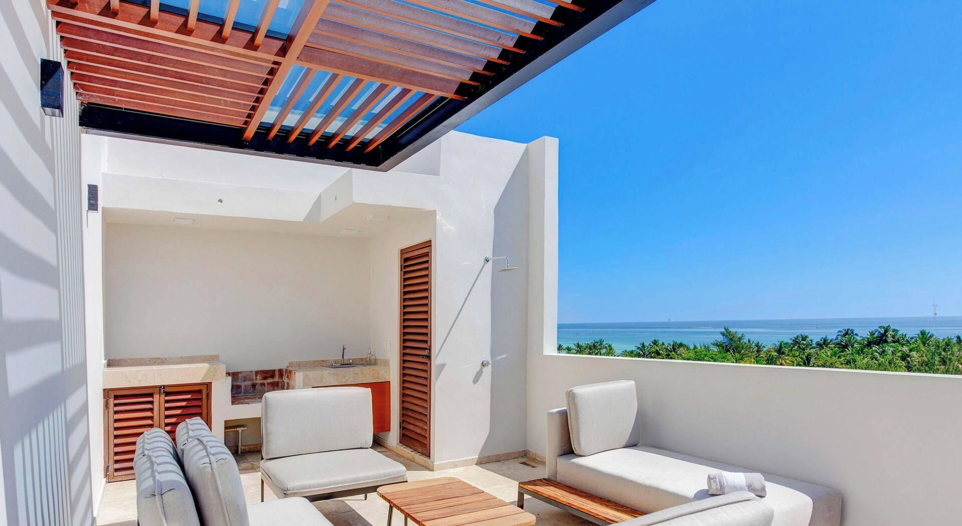 A balcony with a view of the sea, a seating area with a table, and a small kitchenette.