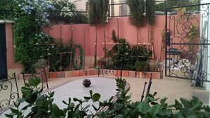 A courtyard with a round table, potted plants, a metal gate, and a red wall with climbing plants. - Cozy Villa in Downtown Agadir (Agadir)
