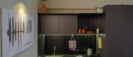 A modern kitchen with a black countertop, a sink, a kettle, and a refrigerator.