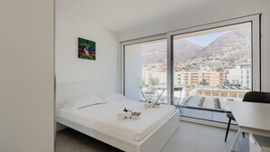 Une chambre moderne avec un lit, un bureau et une grande fenêtre donnant sur la ville.