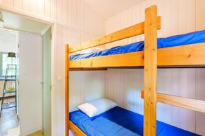 Ein Etagenbett mit blauer Matratze und weißem Kopfkissen in einem Zimmer mit weiß getäfelten Wänden.