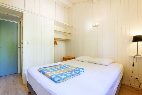 Ein Schlafzimmer mit einem Bett, einem Nachttisch, einer Lampe, einem Kleiderschrank und einer Tür.