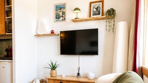 A cozy living room with a flat-screen TV, a comfortable armchair, a wooden coffee table, and a small side table with a plant. - Thémis 112 - The Alpine Cocoon (La Plagne Tarentaise)