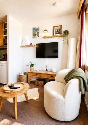 A cozy living room with a flat-screen TV, a comfortable armchair, a wooden coffee table, and a small side table with a plant. - Thémis 112 - The Alpine Cocoon (La Plagne Tarentaise)