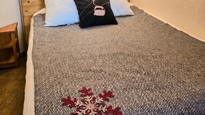 A bed with a gray blanket and a red snowflake design, two white pillows, a black pillow with a ski icon, wooden headboard, and two wall-mounted lights. - Thémis 112 - The Alpine Cocoon (La Plagne Tarentaise)