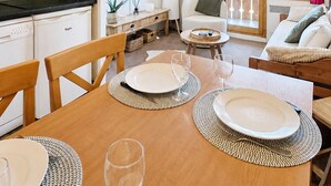 A dining area with a wooden table set for four, a television, and a view of a mountainous landscape through large windows. - Thémis 112 - The Alpine Cocoon (La Plagne Tarentaise)