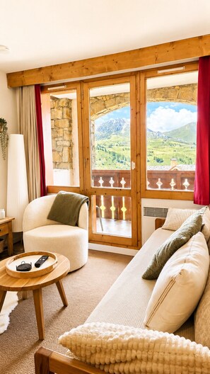 A cozy living room with a sofa, a chair, a small table with a tray, and a view of a mountainous landscape through large windows. - Thémis 112 - The Alpine Cocoon (La Plagne Tarentaise)