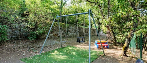 Un espai de jocs amb cadira d'oscil·lació, un banc i una estructura per escalar.