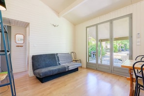 A room with a sofa, a table, and a chair. There is a door with a mirror and a microwave on the wall. - Chalet 'Confort Piscine Partagée' with pool, shared terrace and Wi-Fi (Les Vans)