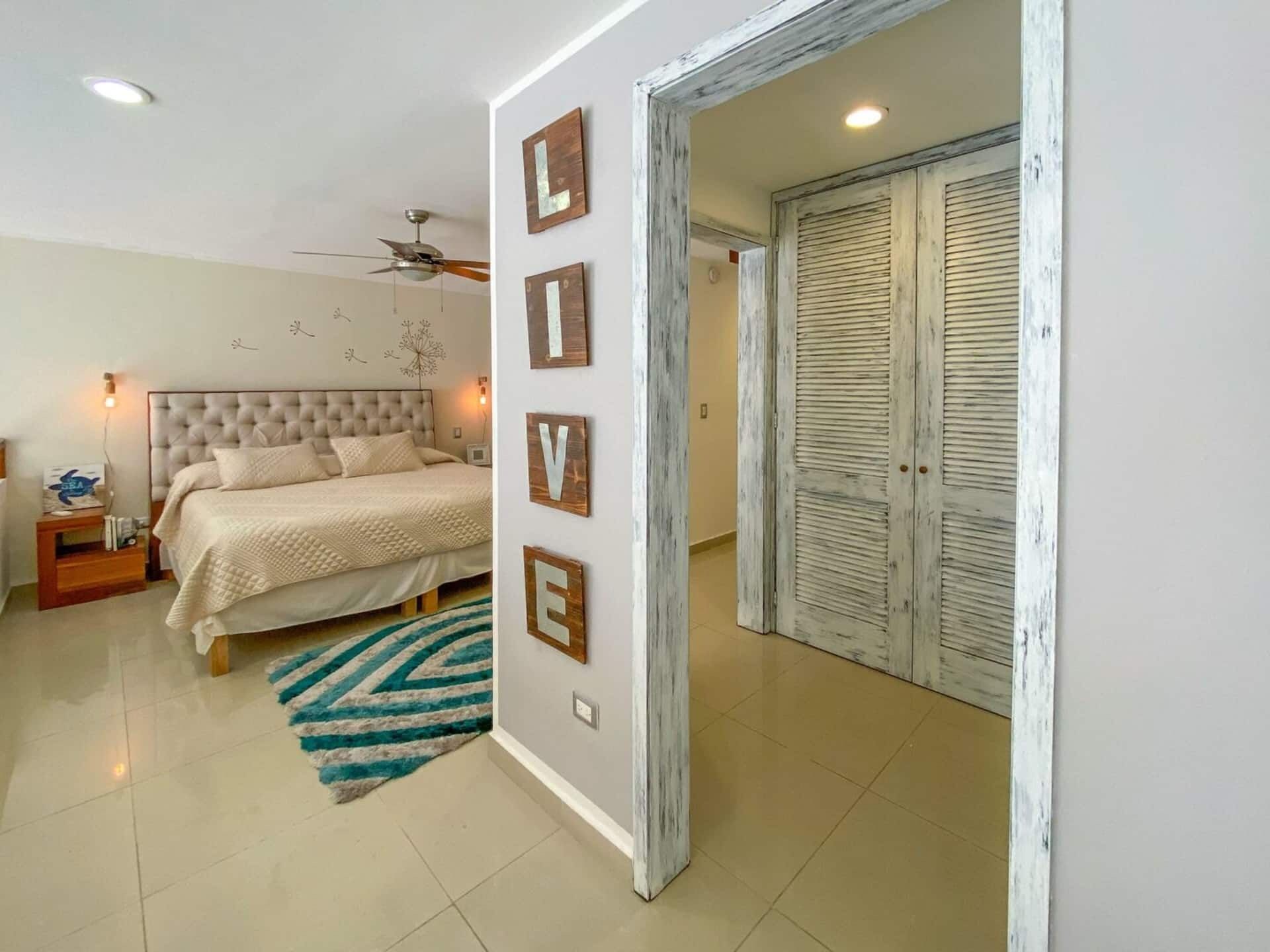 A bedroom with a bed, nightstands, a ceiling fan, and a wall with decorative letters.