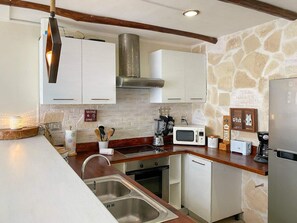 A modern kitchen with white cabinets, a stone wall, a built-in stove, and a stainless steel sink. - Playa retreat w/ pool - walk to ruins, beach & 5th (Playa del Carmen)