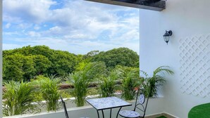 Um pátio externo com mesa e cadeiras, luminária fixada na parede e vista para uma área arborizada.
