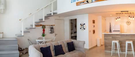 A modern living room with a sofa, a dining area, and a kitchen.