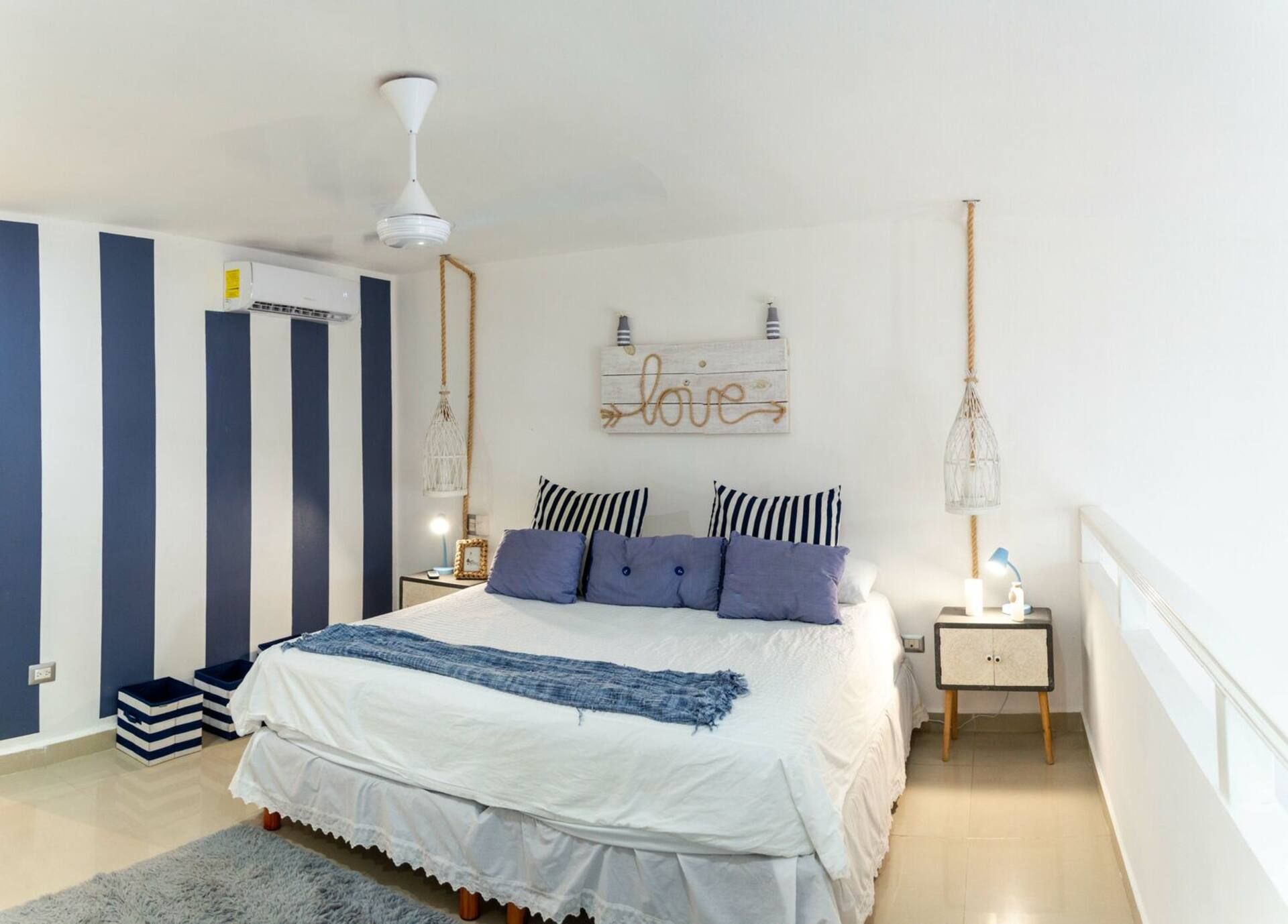 Een slaapkamer met een bed, nachtkastjes, een hanglamp, een bord aan de muur en een plafondventilator.