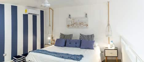 A bedroom with a bed, bedside tables, a hanging light fixture, a wall-mounted sign, and a ceiling fan.