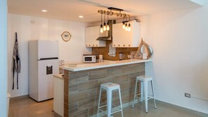 Cozinha moderna com geladeira branca, micro-ondas e bancada de madeira com banquetas.
