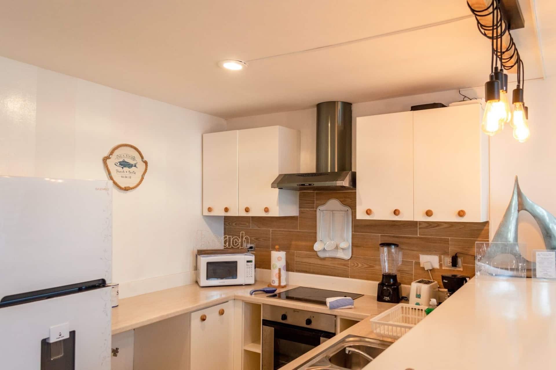 A modern kitchen with white cabinets, a stainless steel range hood, a microwave, and a blender on the counter.
