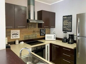 Eine moderne Küche mit dunklen Holzschränken, einem Edelstahlkühlschrank, einer Mikrowelle und einer Kaffeemaschine.