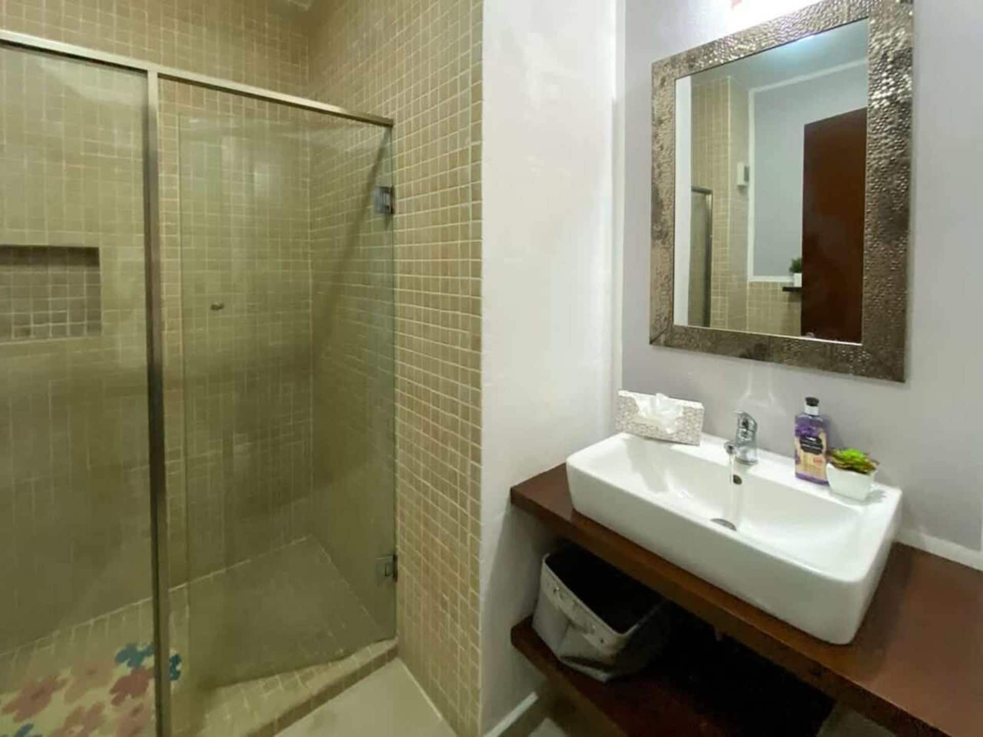 Een badkamer met een douchecabine van glas, een wit wastafelmeubel met een spiegel erboven en een klein plankje met toiletartikelen.
