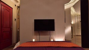 A hotel room with a bed, a television mounted on the wall, and a red door. - Deluxe Loft at Le Moulin Vert (Paris)