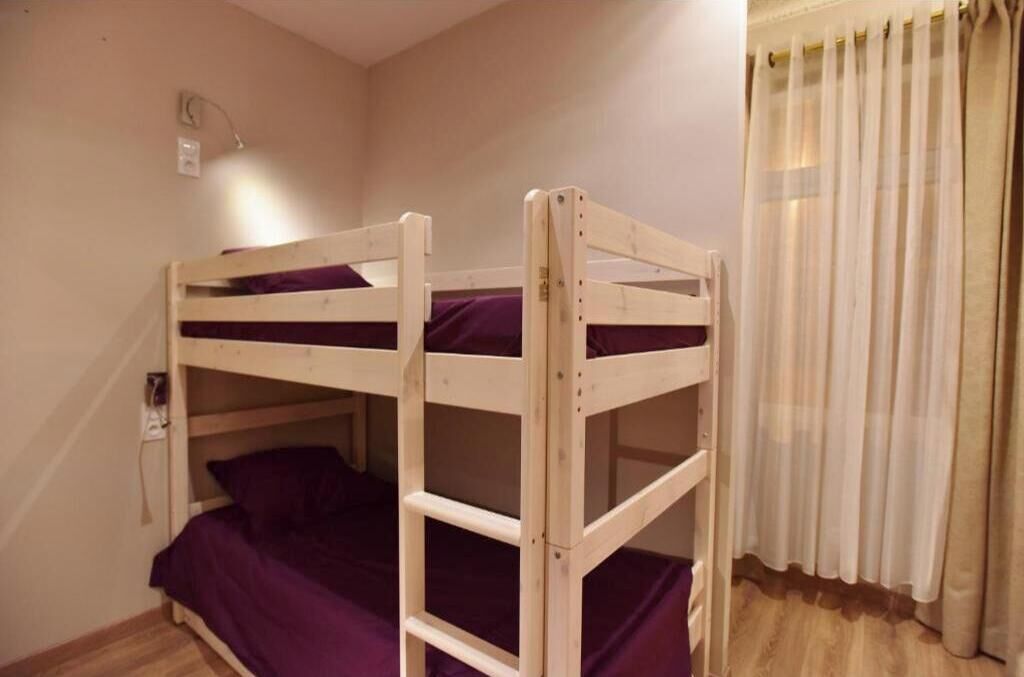 Un lit superposé avec un matelas violet, une prise de courant et une fenêtre avec des rideaux.