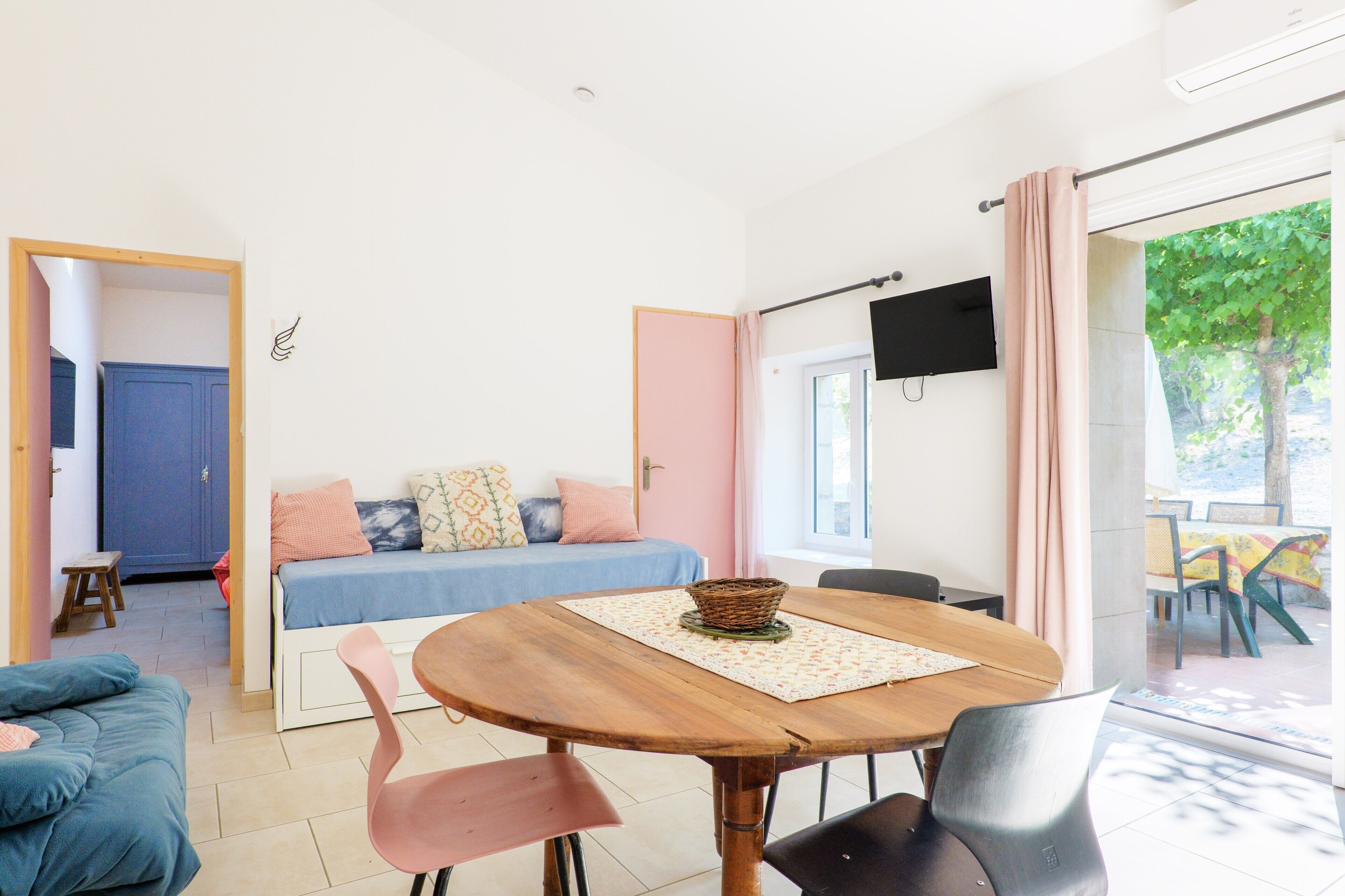 Une pièce comprenant un lit, une table avec des chaises, un téléviseur et une fenêtre avec des rideaux.