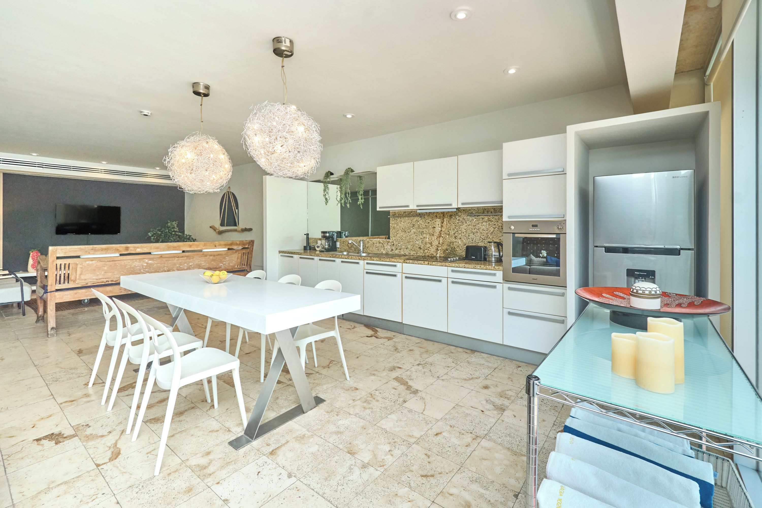Eine moderne Küche mit weißen Schränken, einem Edelstahl-Kühlschrank und einem Essbereich mit weißem Tisch und Stühlen.