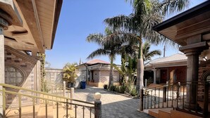 A courtyard with a tiled walkway, palm trees, and a building with a tiled roof.