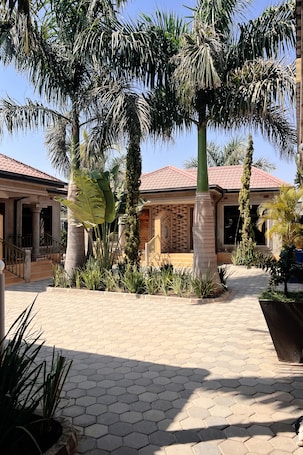 A courtyard with palm trees, a tiled walkway, and a building with a red roof.