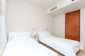 A hotel room with two single beds, a bedside table with a lamp, a wooden door, and a white wall. - Magia resort condo w/ pool & balcony (Playa del Carmen)
