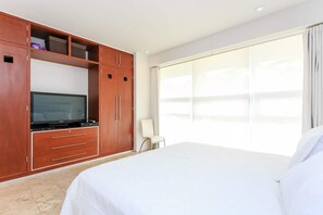 A hotel room with a large bed, a TV on a wooden cabinet, a chair, and a large window. - Magia resort condo w/ pool & balcony (Playa del Carmen)