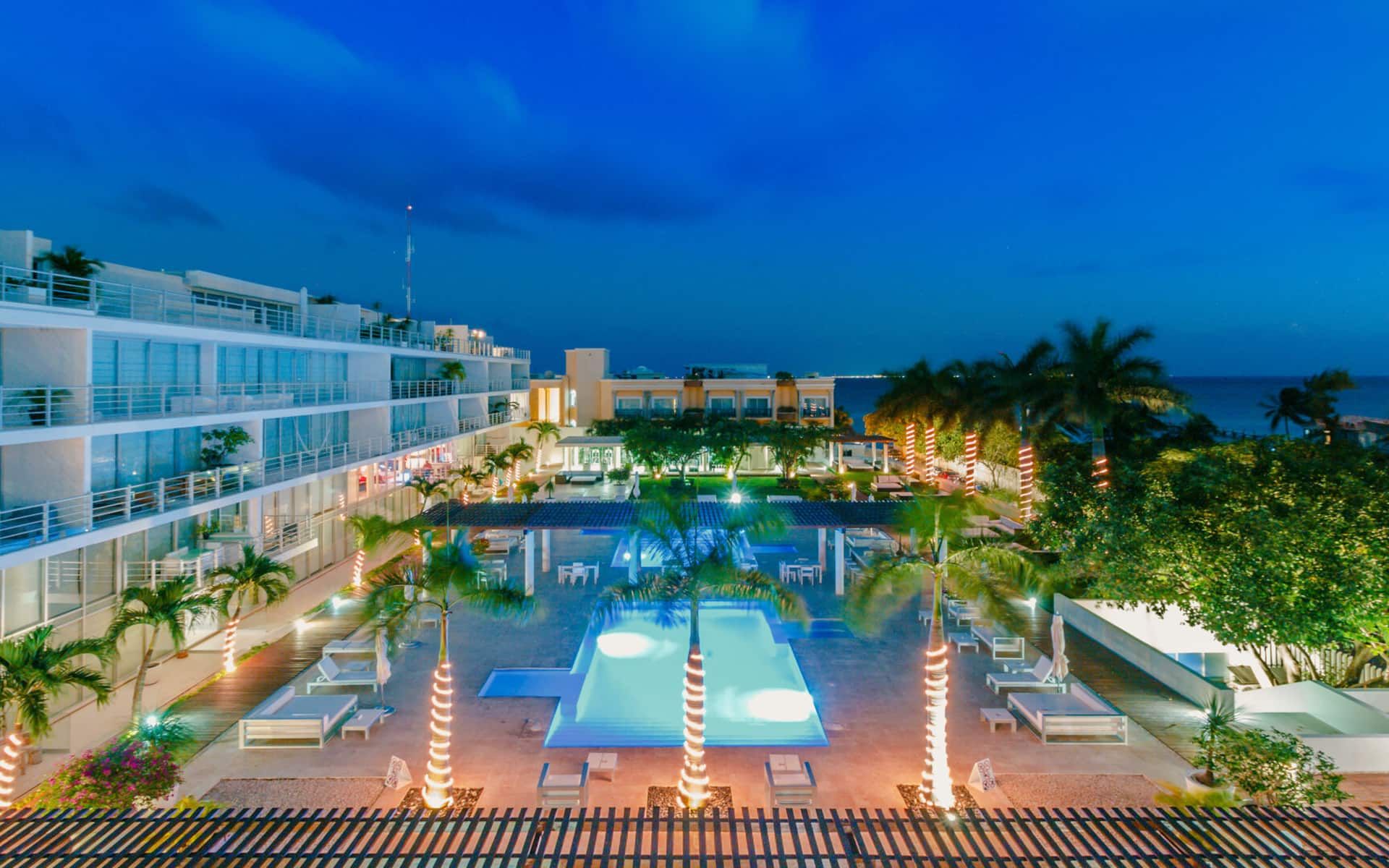 A hotel pool area with multiple levels, palm trees, and a view of the ocean at dusk.